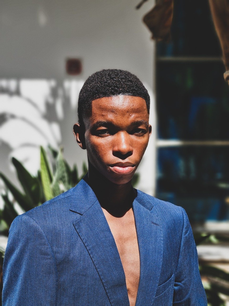 close-up portrait, black male model, fierce stare, intense expression, blue suit, fashion close-up, dominant look, editorial headshot, bold gaze, male model close-up, high fashion, strong facial expression, fashion editorial, confident face, stylish man