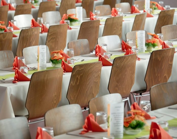 Beautifully arranged tables with wooden chairs for a formal event, adorned with orange flowers.
