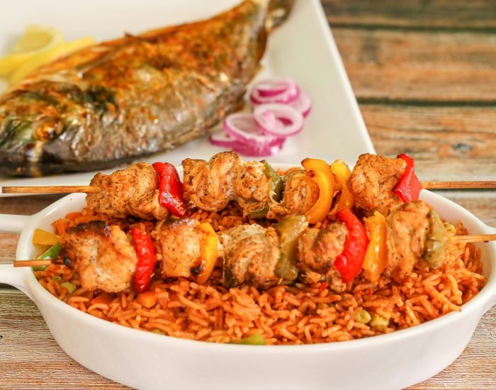 Close-up of flavorful Nigerian jollof rice with grilled chicken skewers and roasted fish.