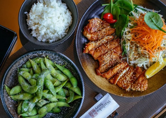 A beautifully presented Japanese meal featuring teriyaki chicken, rice, salad, and edamame.