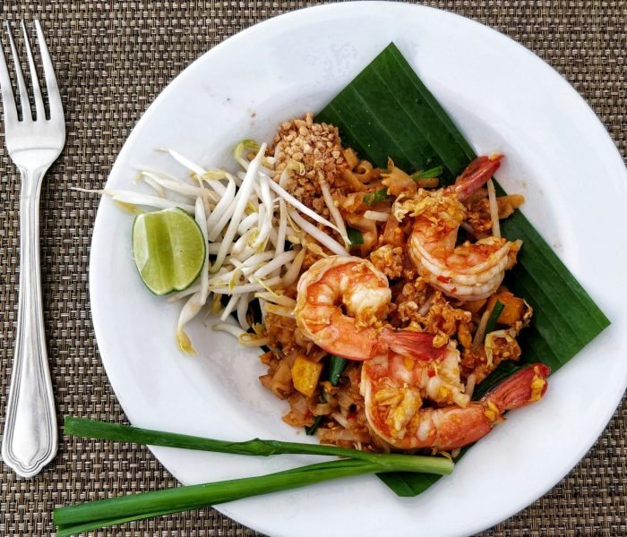 Delicious Pad Thai with shrimps, bean sprouts, and lime on a banana leaf, served on a woven mat.