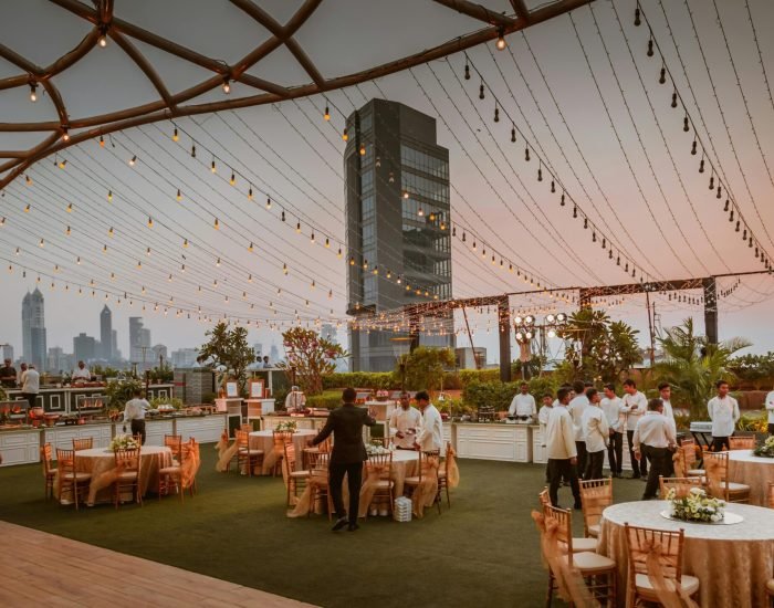 Elegant rooftop event with tables and lights set against Mumbai skyline at sunset, India.