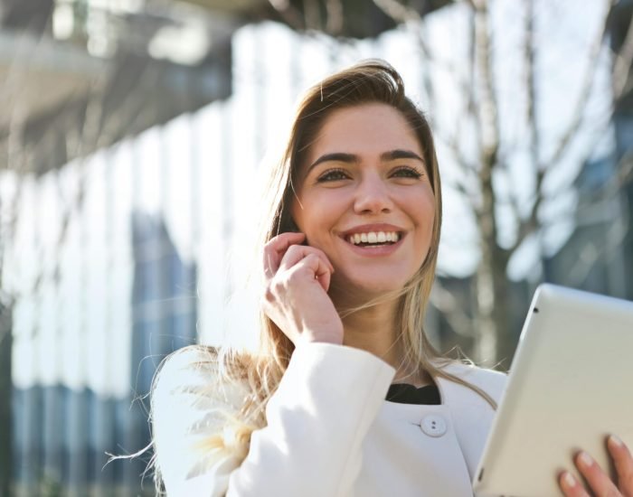 Confident businesswoman using her tablet and phone, smiling outdoors in sunlight.